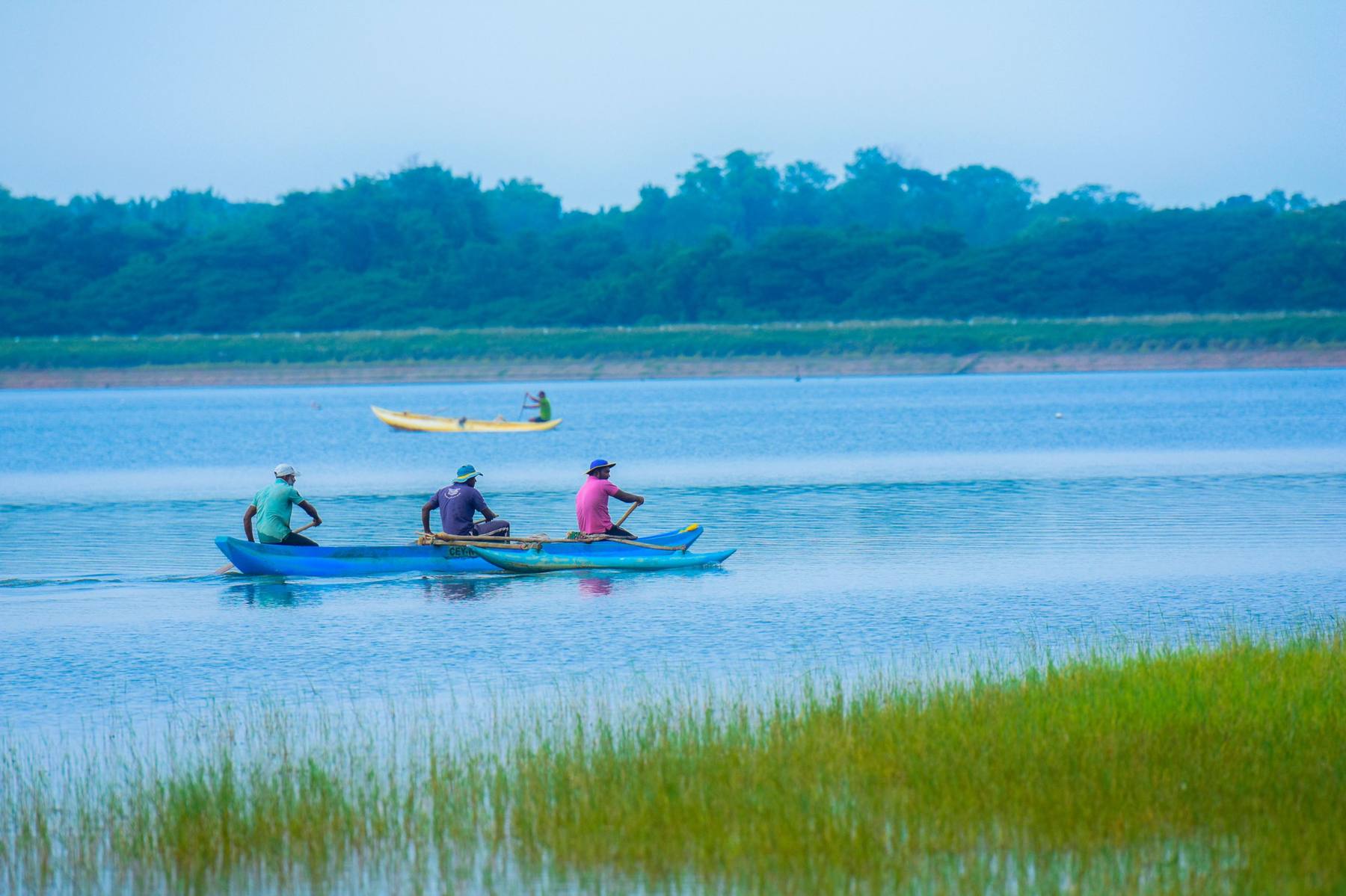 Fishermen paddling an outrigger canoe across a calm lake